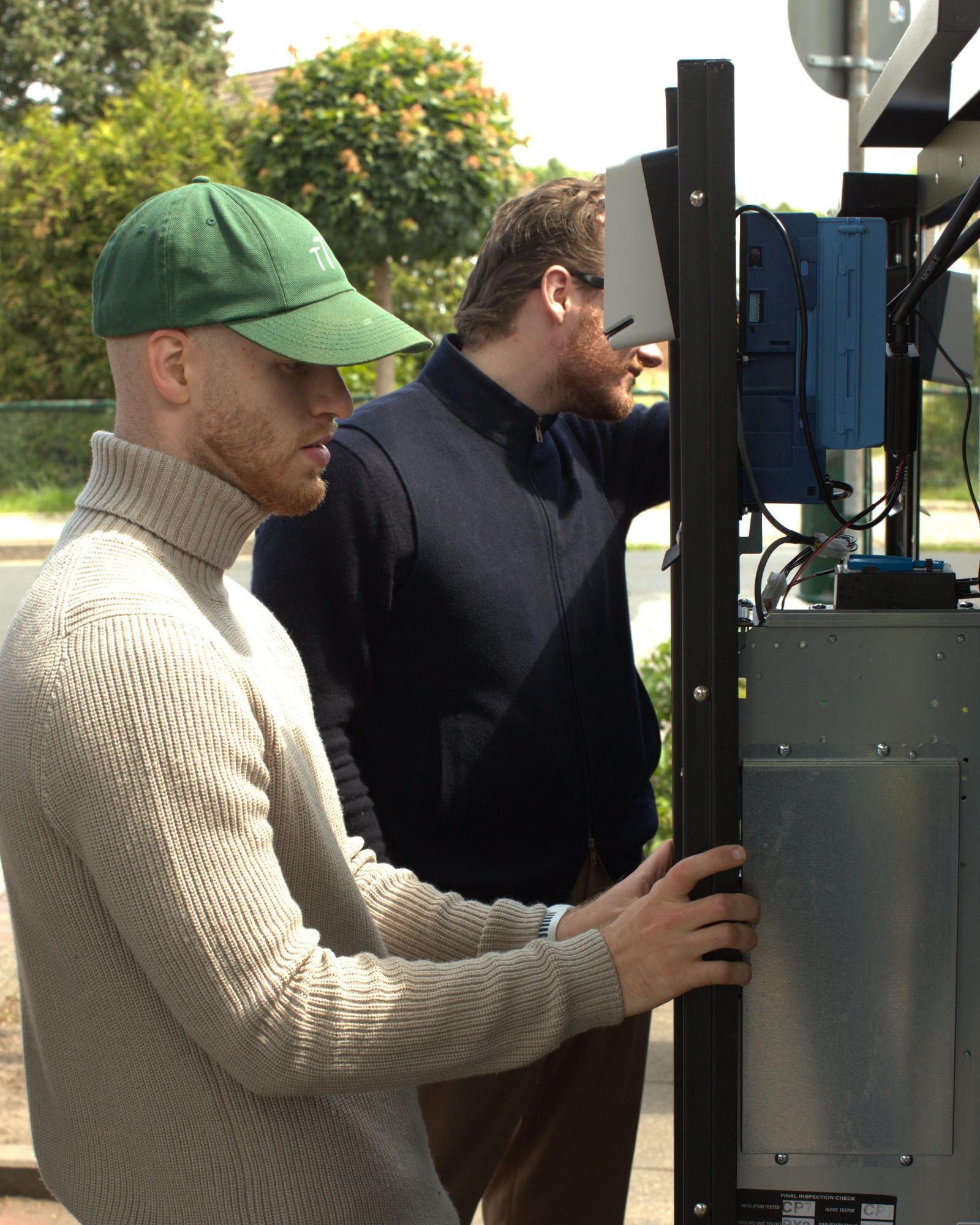 Zwei Männer führen Wartungsarbeiten an der geöffneten Technik eines Verkaufsautomaten durch.