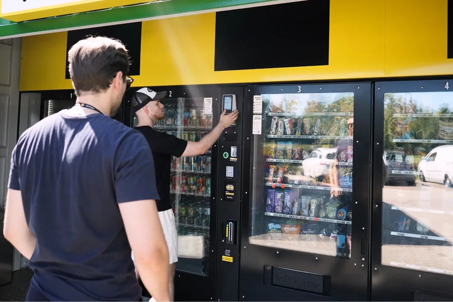 Eine Person erklärt einem Kollegen die Bedienung des Terminals an einem Automatenstandort.